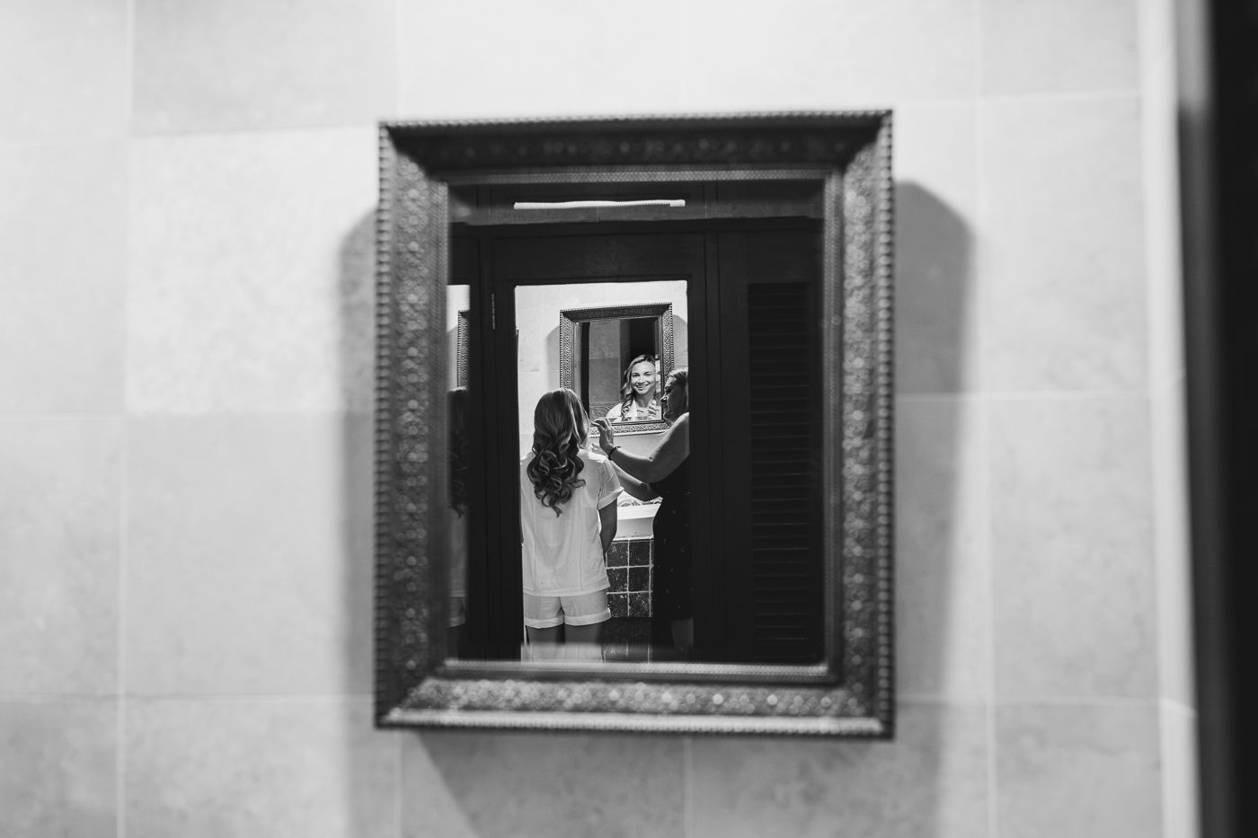 Black and white photo of two children reflected in an ornate framed mirror mounted on a wall.