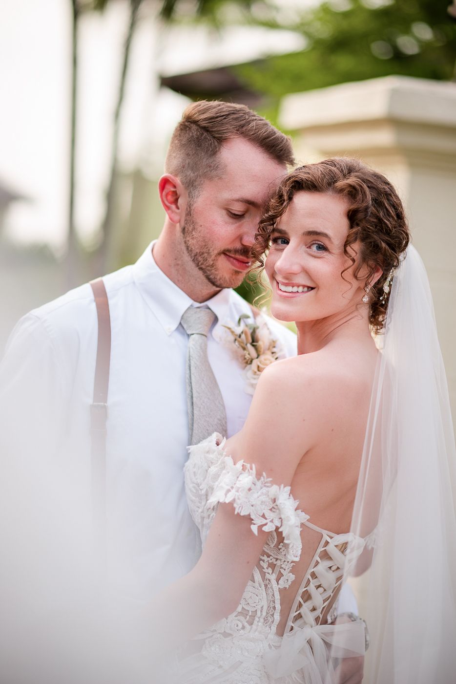 Close-up wedding portraits against soft white background with tropical elements.
