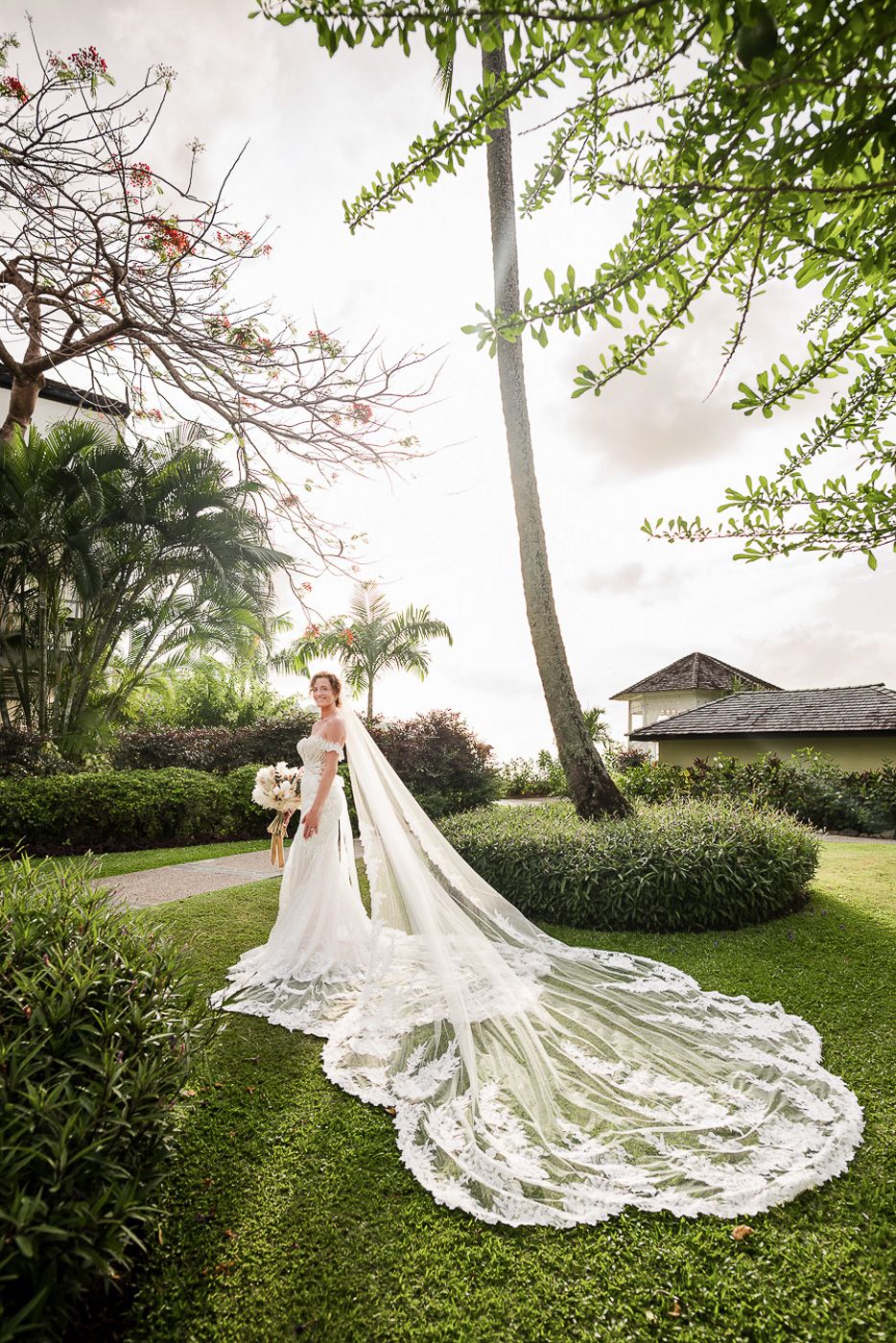 Dramatic wedding dress with long lace train photographed in a lush garden setting.