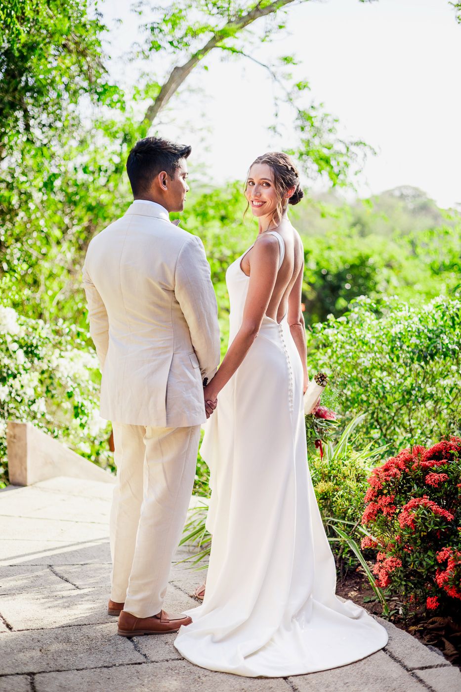 Wedding couple shares tender moments while walking along a scenic garden path with blooming flowers.