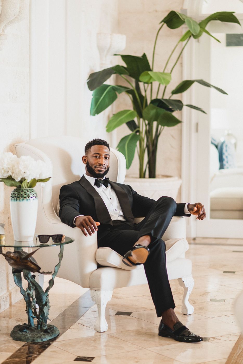 Formal portrait in a luxury interior setting with large plants and white decor elements.