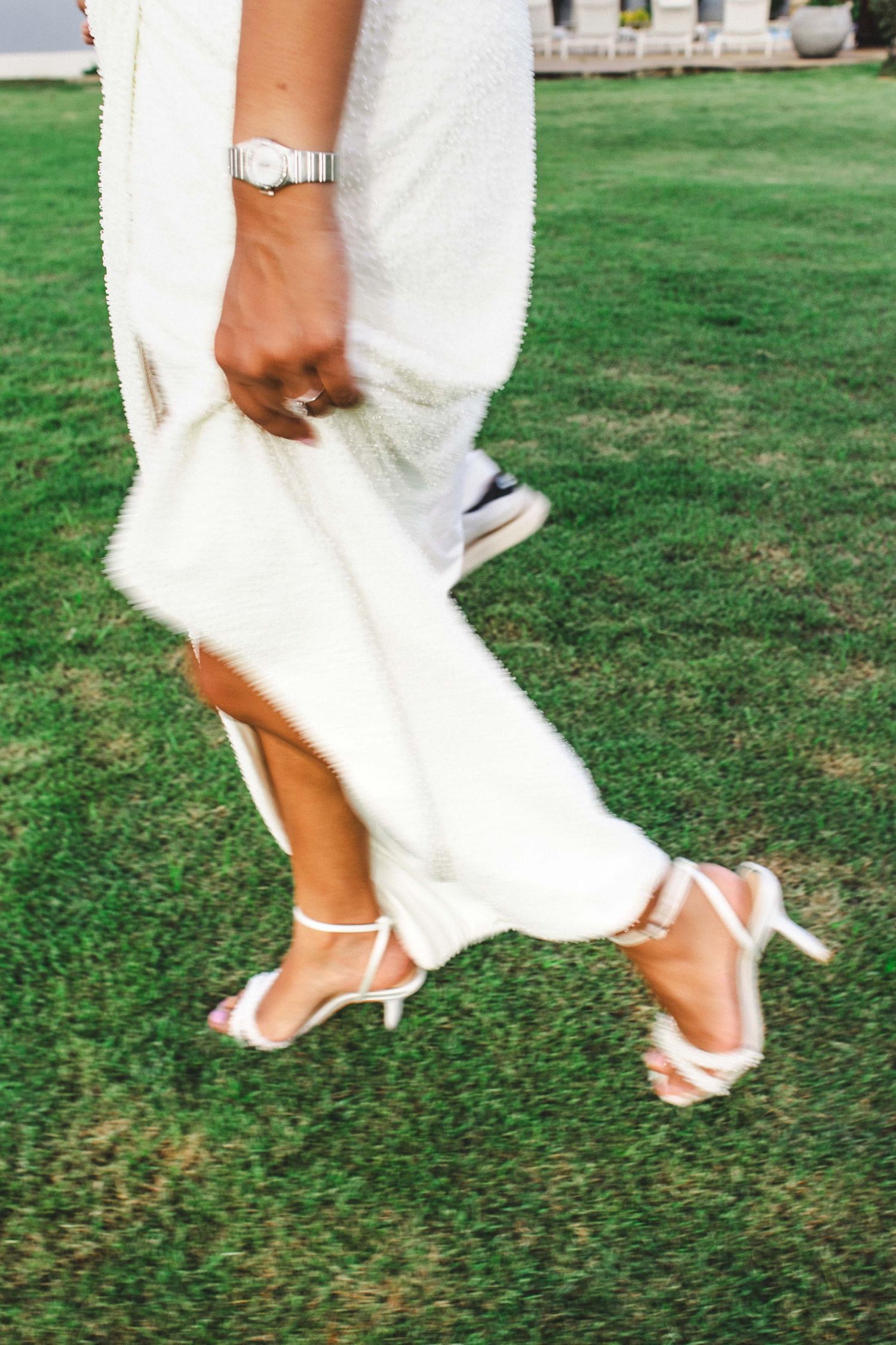 Close-up of bride's feet in white heels walking on grass during a wedding celebration.