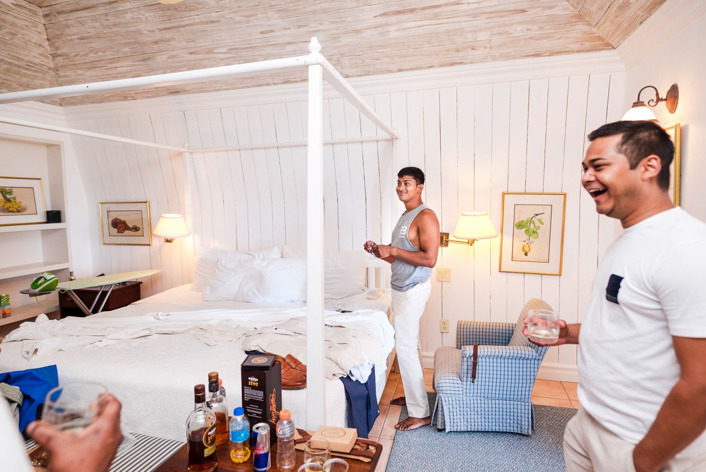 Pre-wedding celebration scene with drinks and festivities in bright coastal-style bedroom.