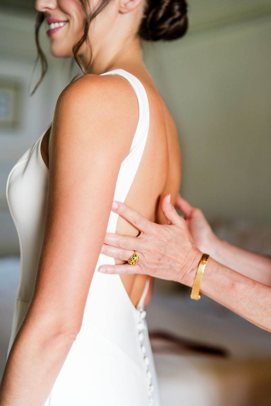 Close-up of hands adjusting the back of an elegant white wedding dress.