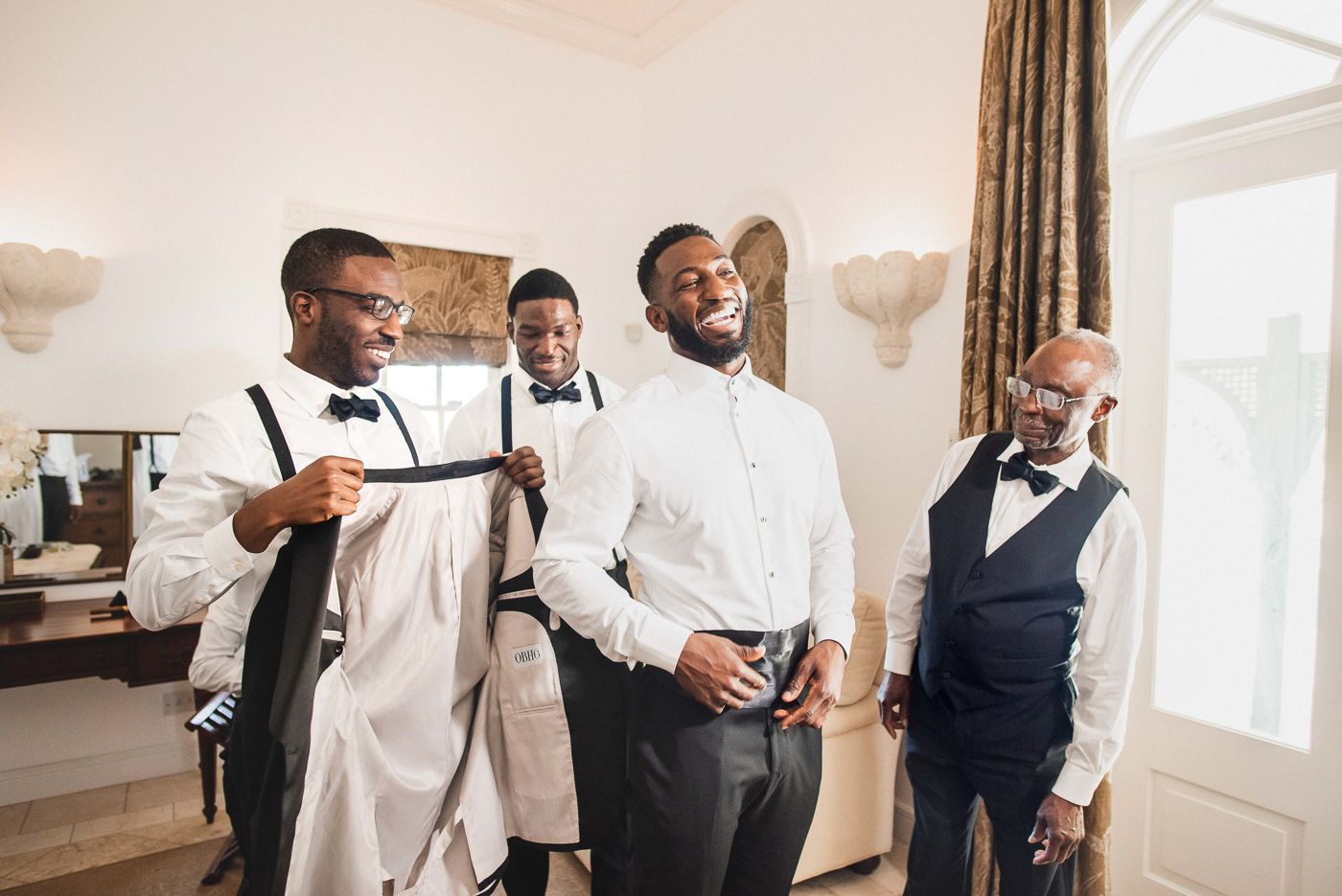 Groomsmen in formal attire prepare for wedding ceremony in bright room.