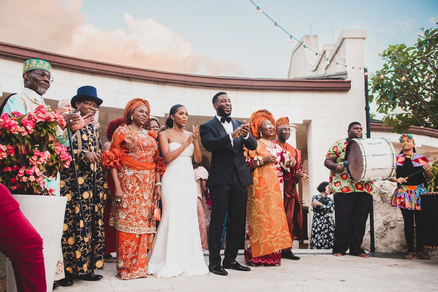 Wedding celebration with guests in vibrant traditional attire gathering for group photos outdoors.