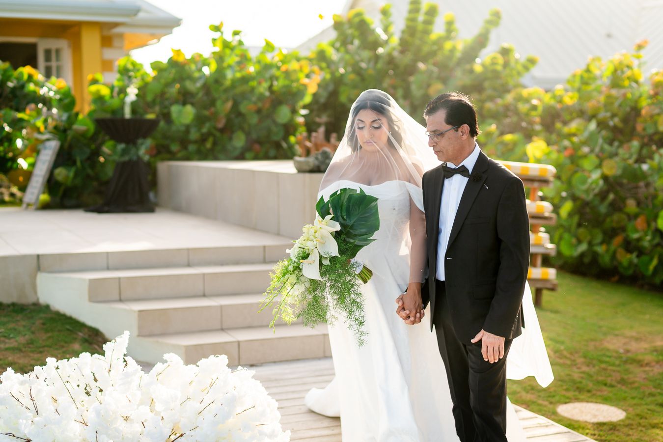 Elegant wedding couple poses on garden steps during golden hour with lush tropical landscaping.