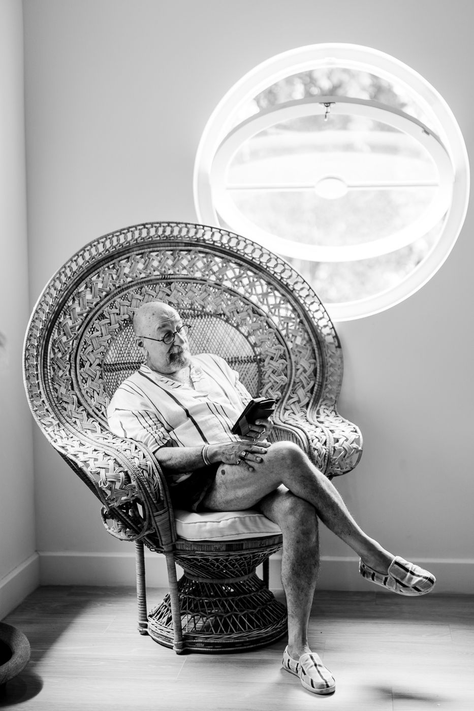 Black and white photo of someone relaxing in an ornate peacock chair under circular lighting.