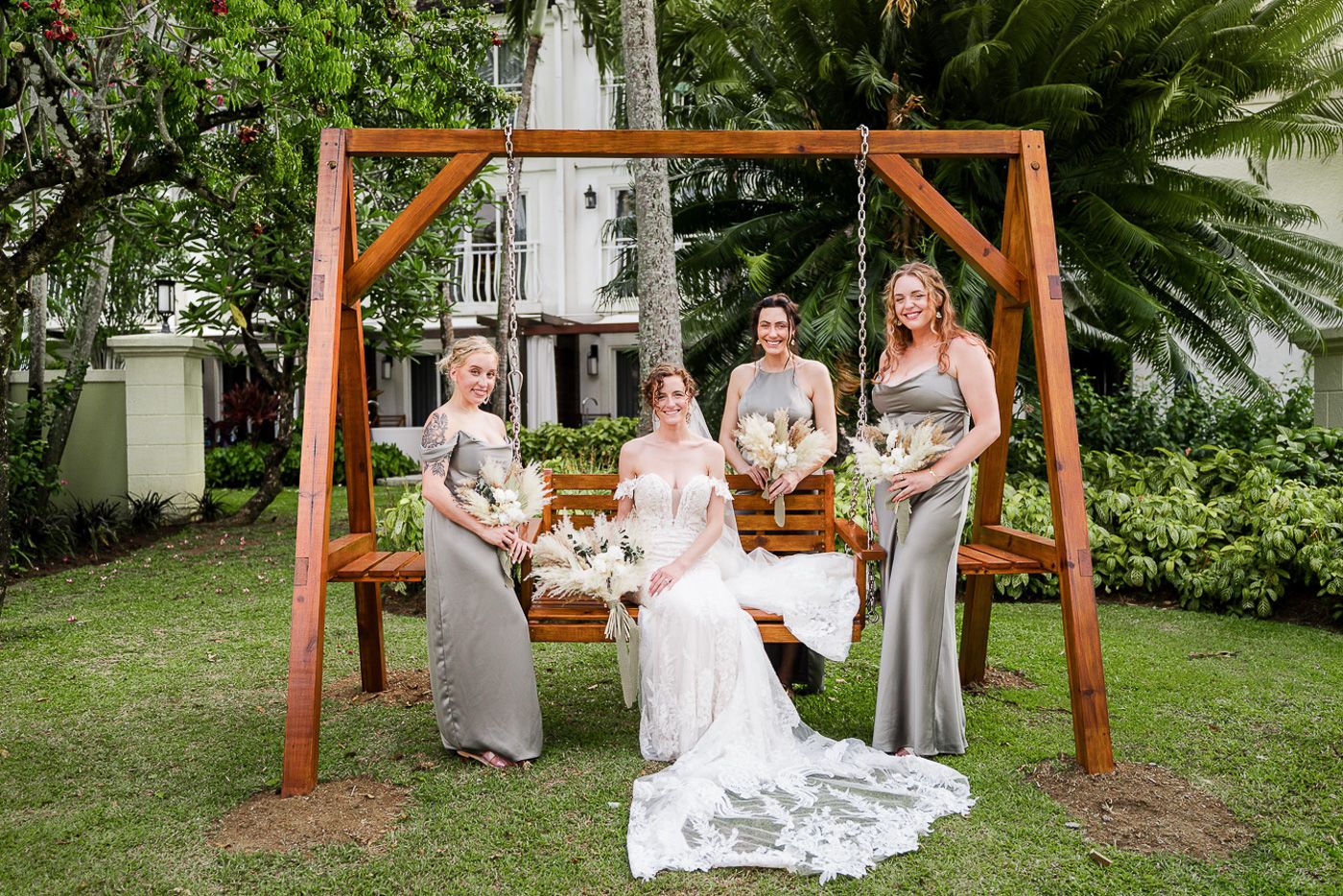 Wedding party gathering under wooden arch with bridesmaids in gray dresses.