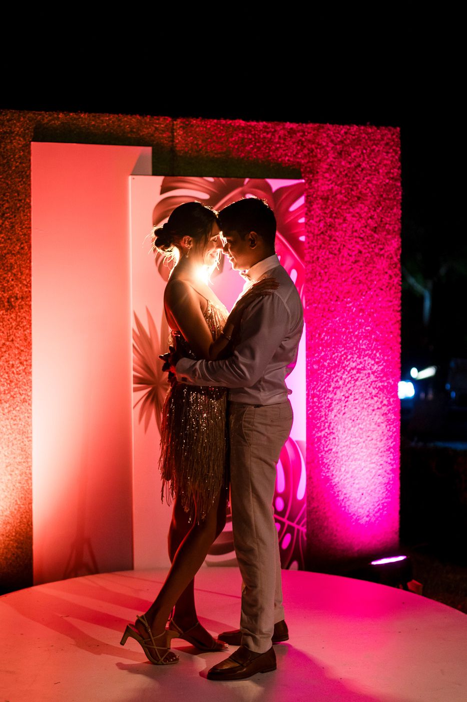 Couple dancing romantically under dramatic pink and red lighting on a dance floor.