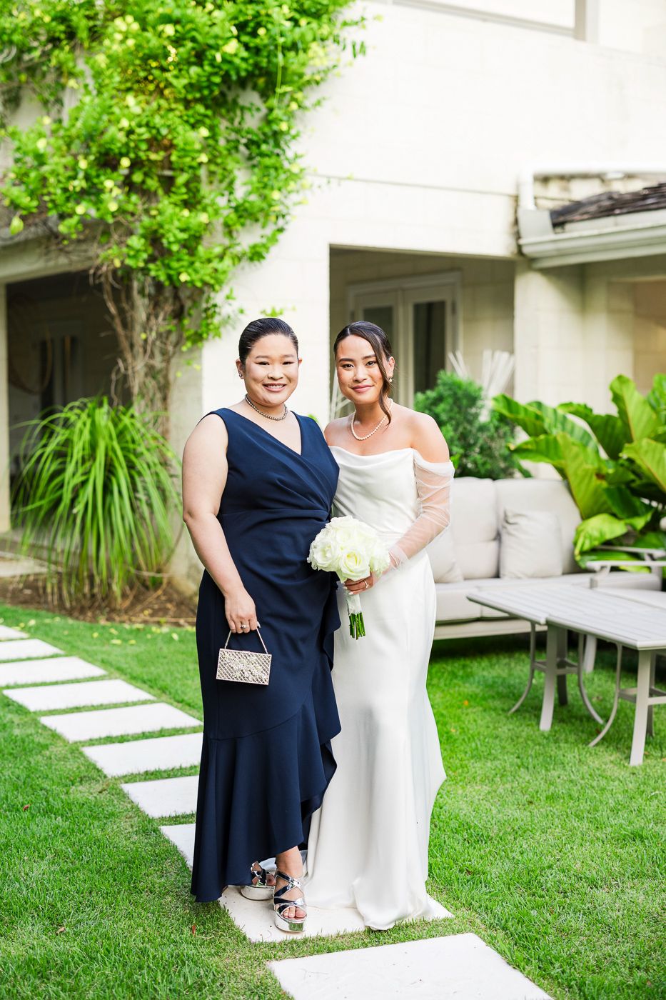 Wedding party poses on manicured lawn with white building and tropical landscaping in background.