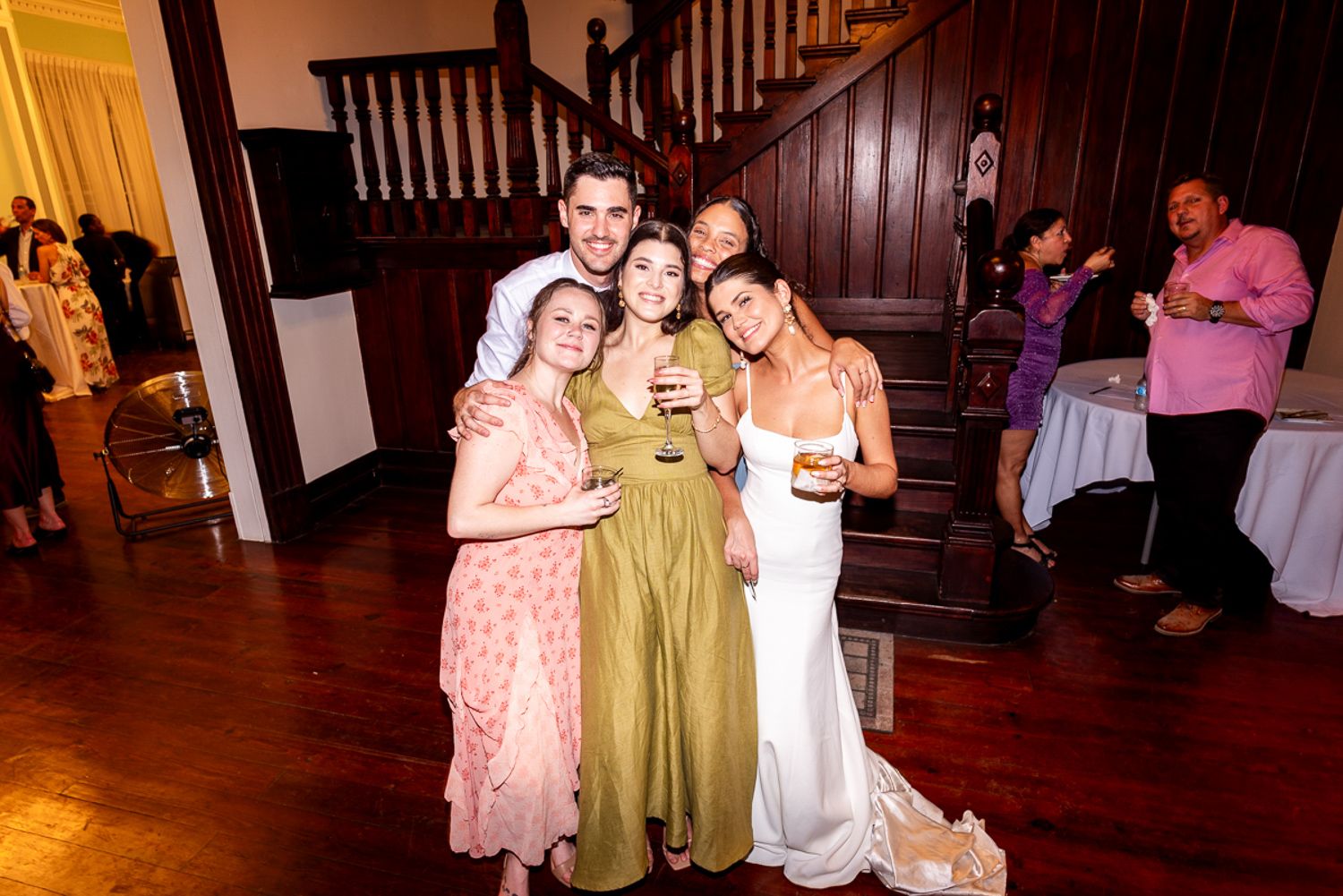 Wedding guests dance on a wooden floor during a reception celebration in a warmly lit venue.
