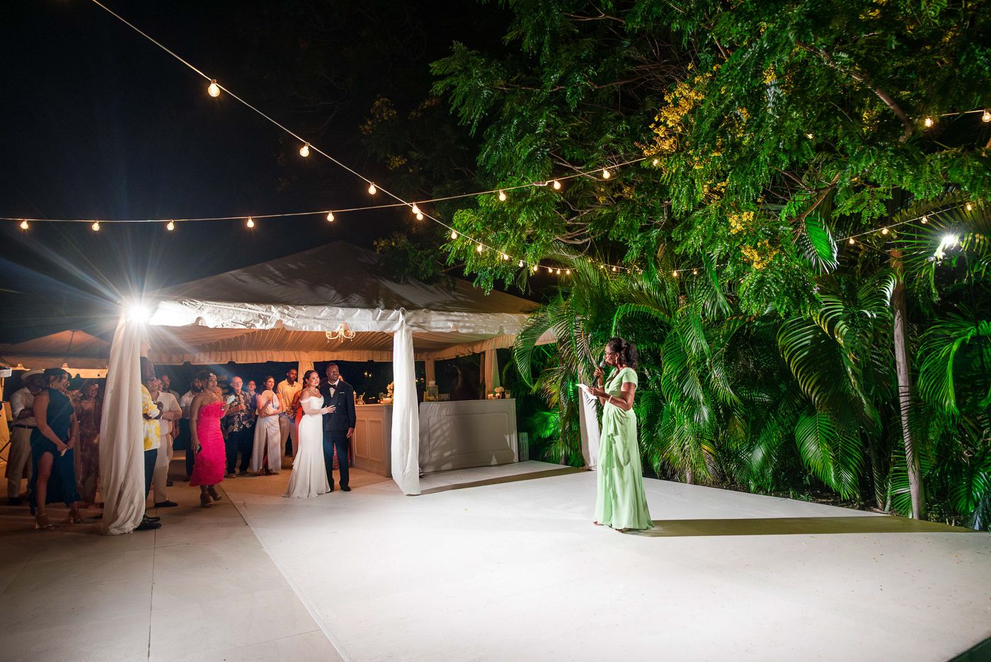 Panoramic view of an evening wedding reception with string lights and palm trees.