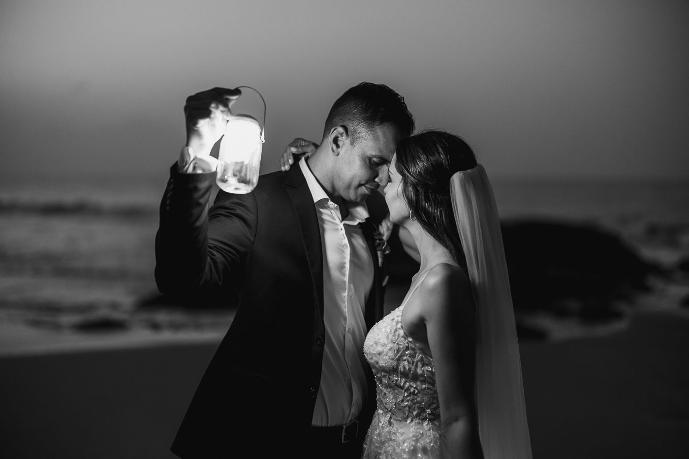 Romantic couple sharing an intimate moment on a beach at night, illuminated by a glowing lantern.