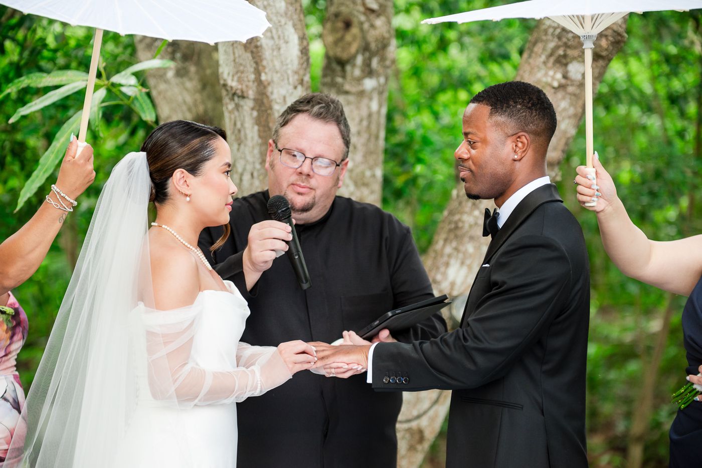 A wedding ceremony features decorative parasols held over the couple during their vow exchange.