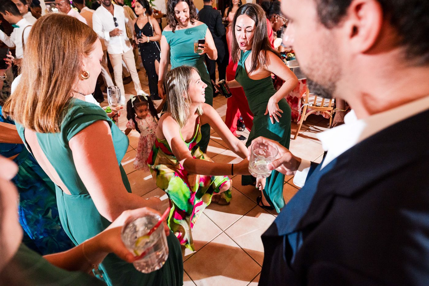 Wedding guests mingle and dance at a lively reception with drinks and vibrant atmosphere.
