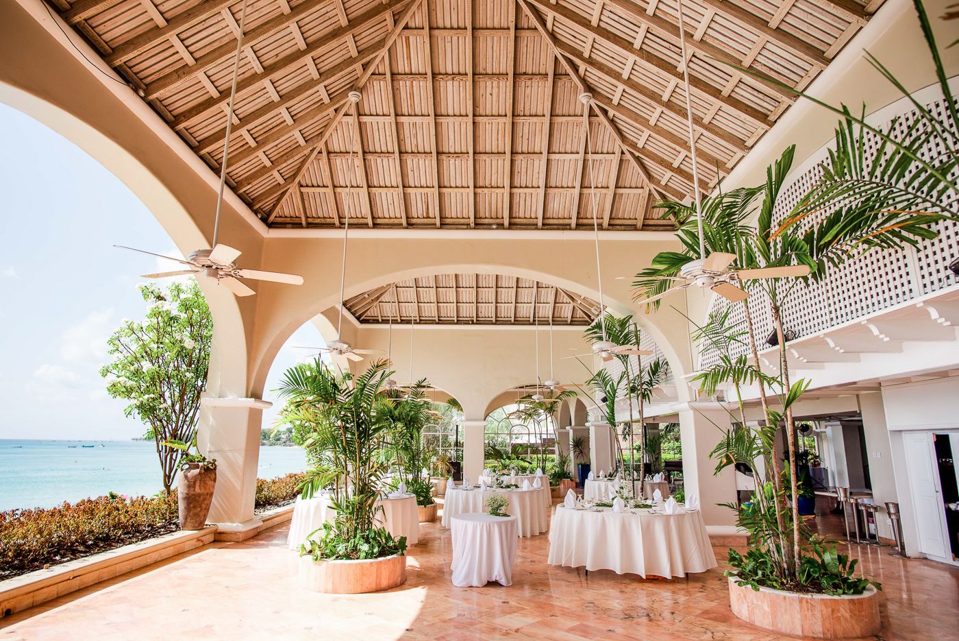 Open-air beachfront venue with vaulted ceilings and elegant white table settings for a tropical event.