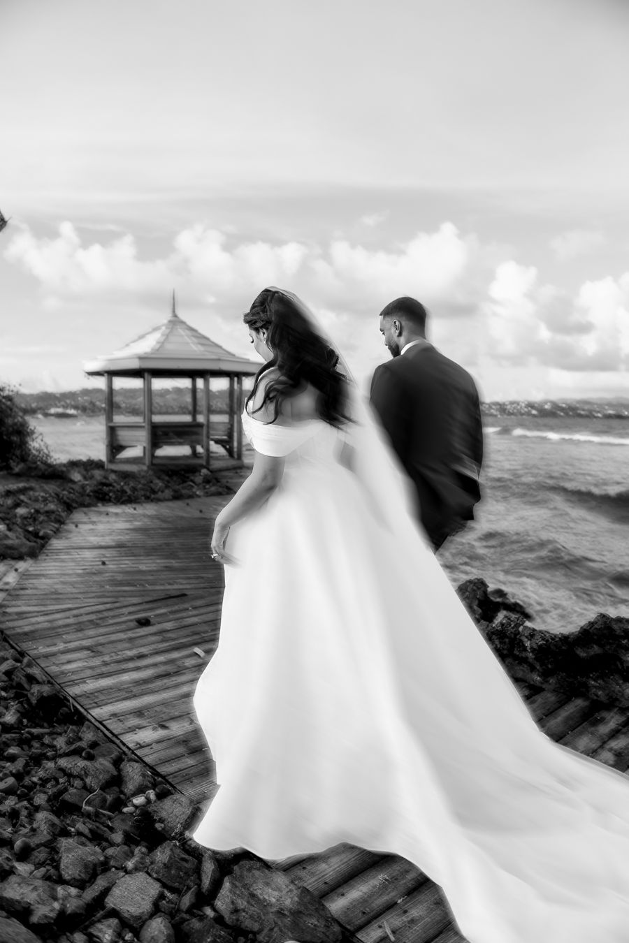 Black and white wedding photos captured on coastal boardwalk with waves crashing.