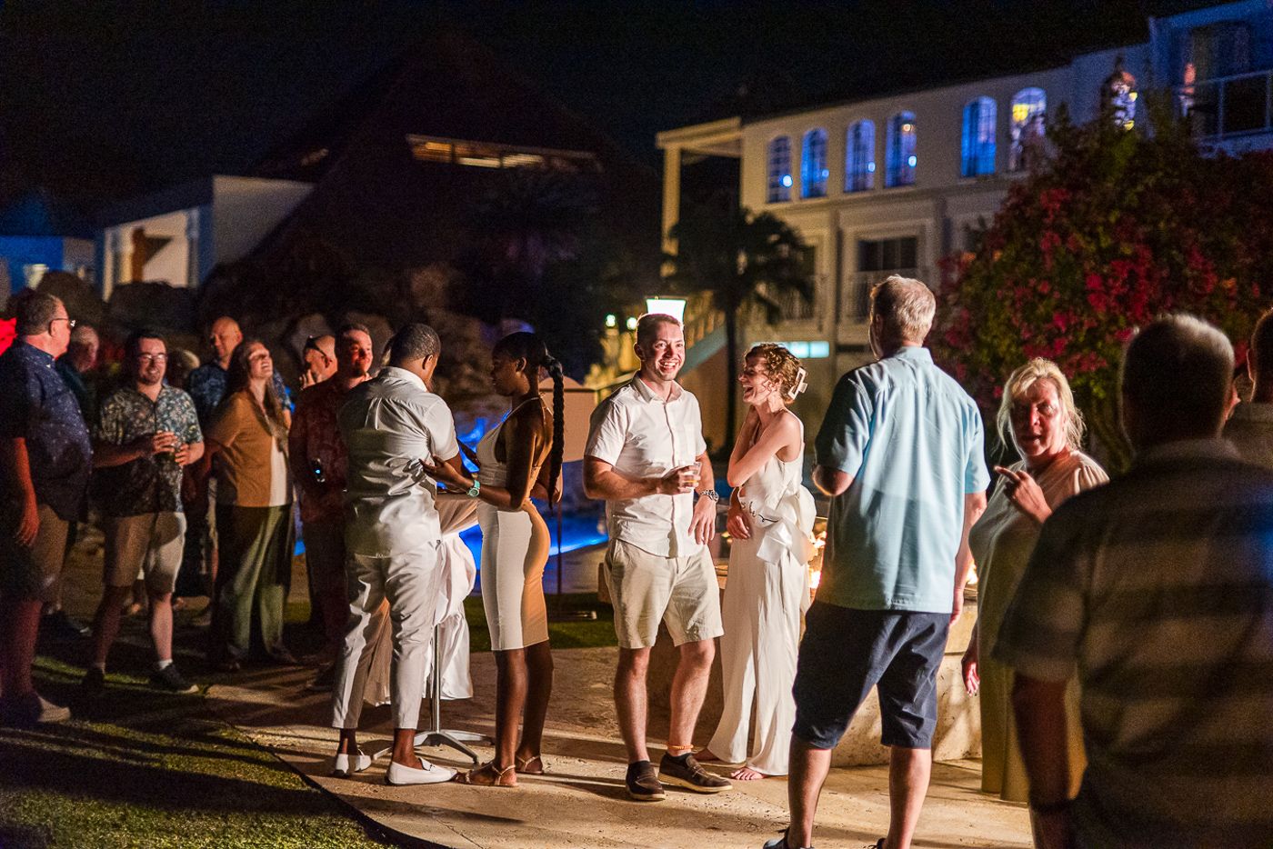 Evening outdoor event with guests mingling on a lawn under string lights.