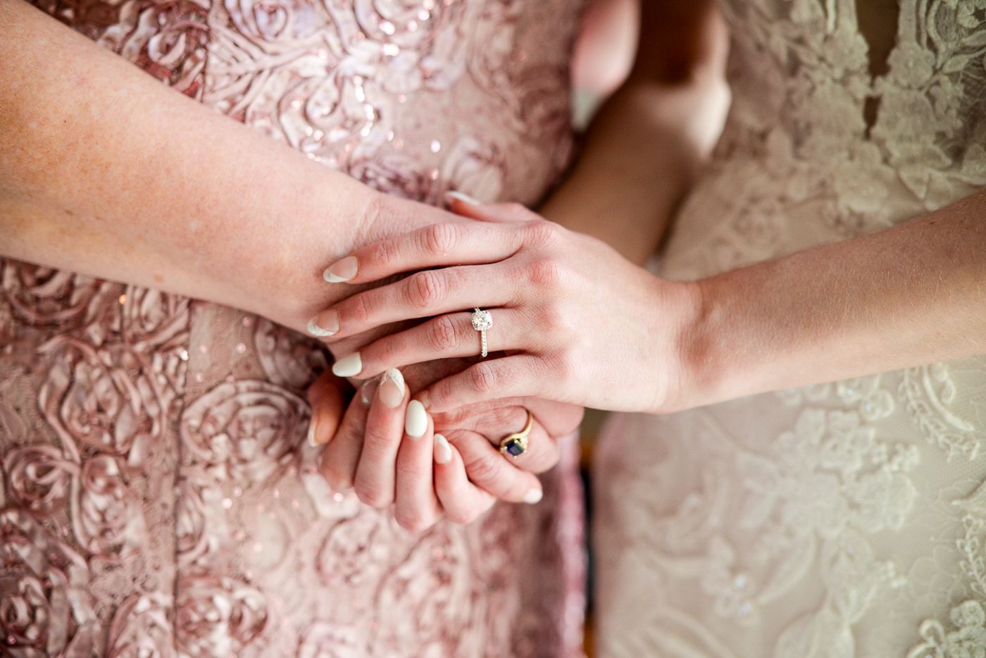 Close-up of hands showing wedding and engagement rings against lace fabric background.