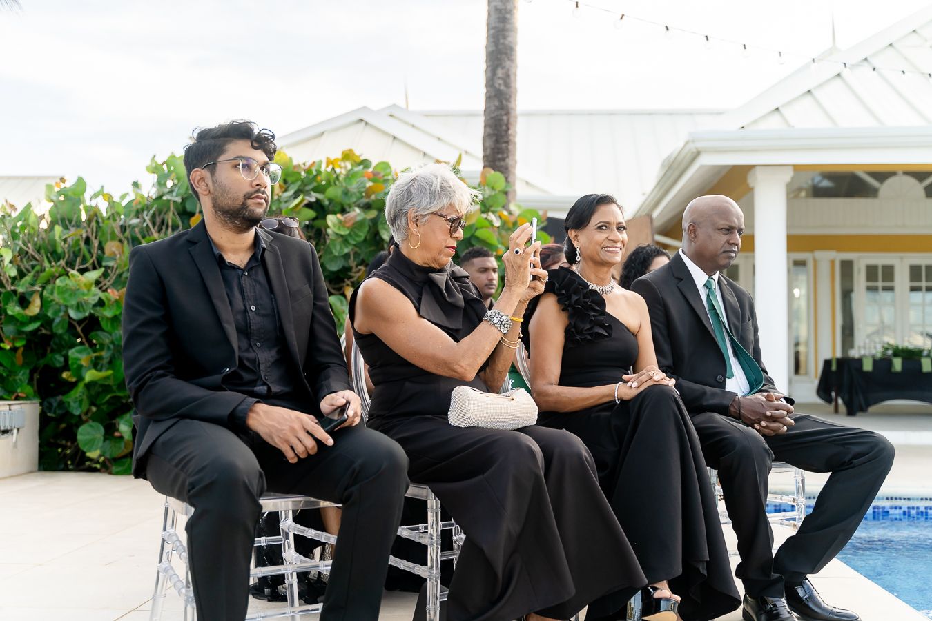 Wedding guests seated poolside in formal attire during outdoor reception.