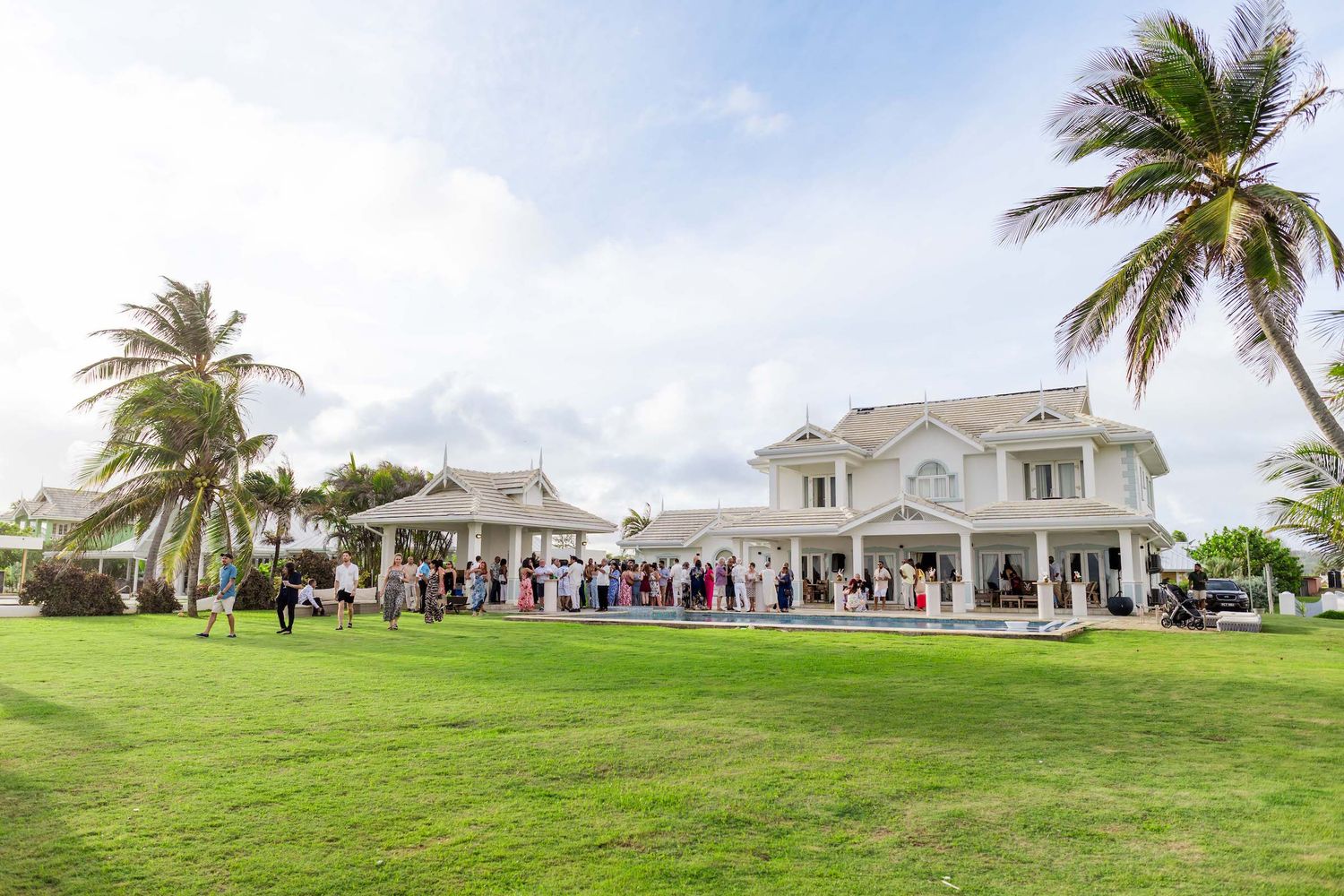 Panoramic view of white event venue with palm trees and guest seating on manicured lawn.