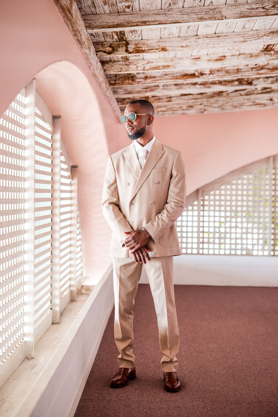 Stylish figure in cream colored suit standing in vintage hallway with window patterns.