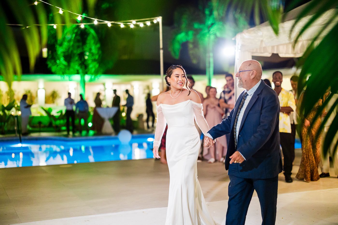 Wedding guests dance and celebrate on an outdoor patio with green uplighting and string lights.