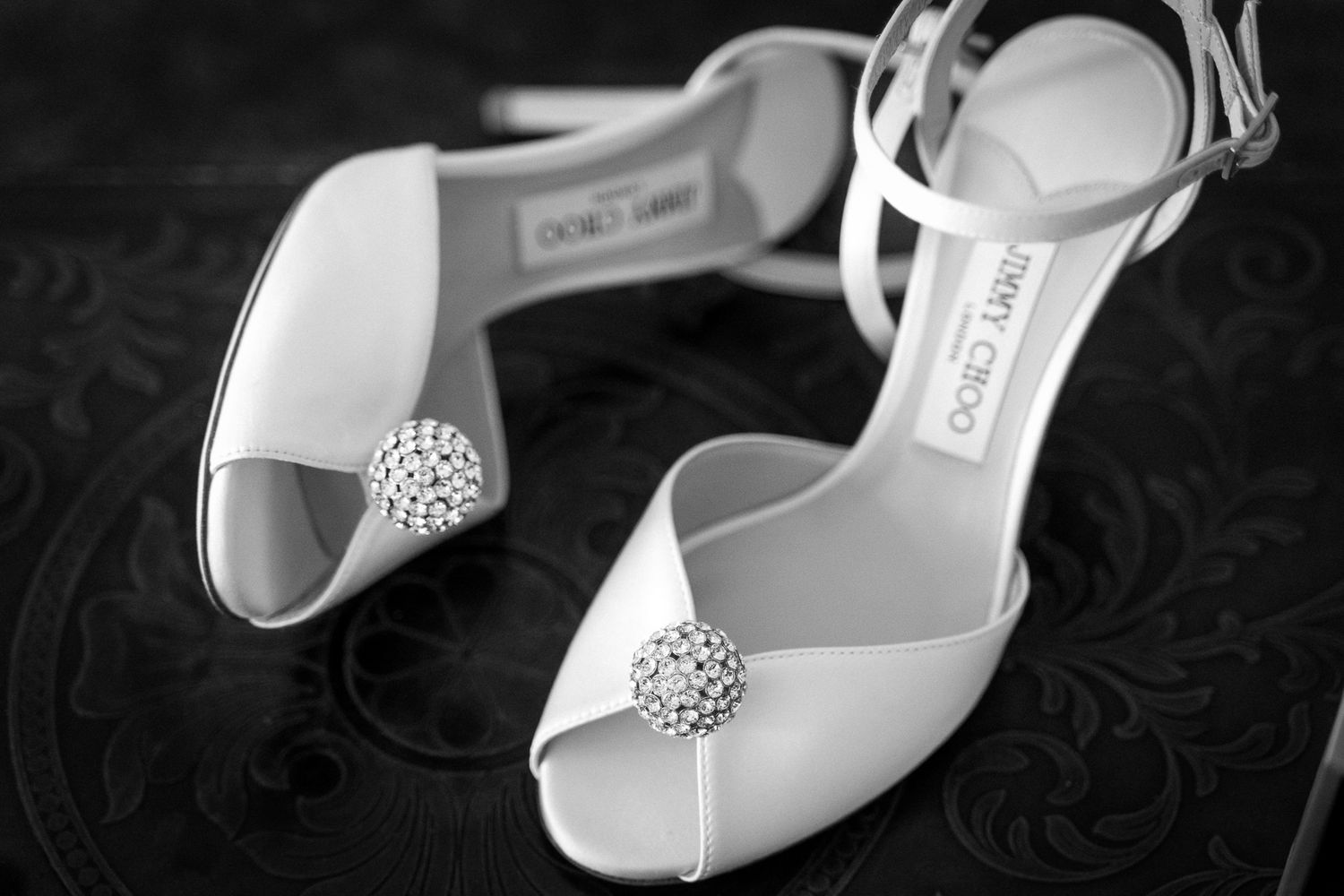 Elegant white bridal shoes with crystal embellishments on dark textured background.