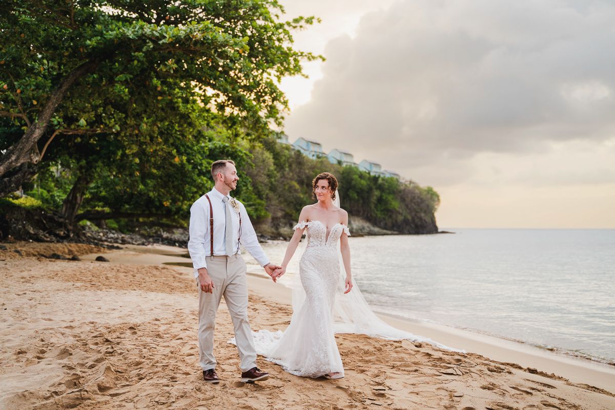 Romantic beach wedding photoshoot with couple walking along tropical shoreline at sunset.
