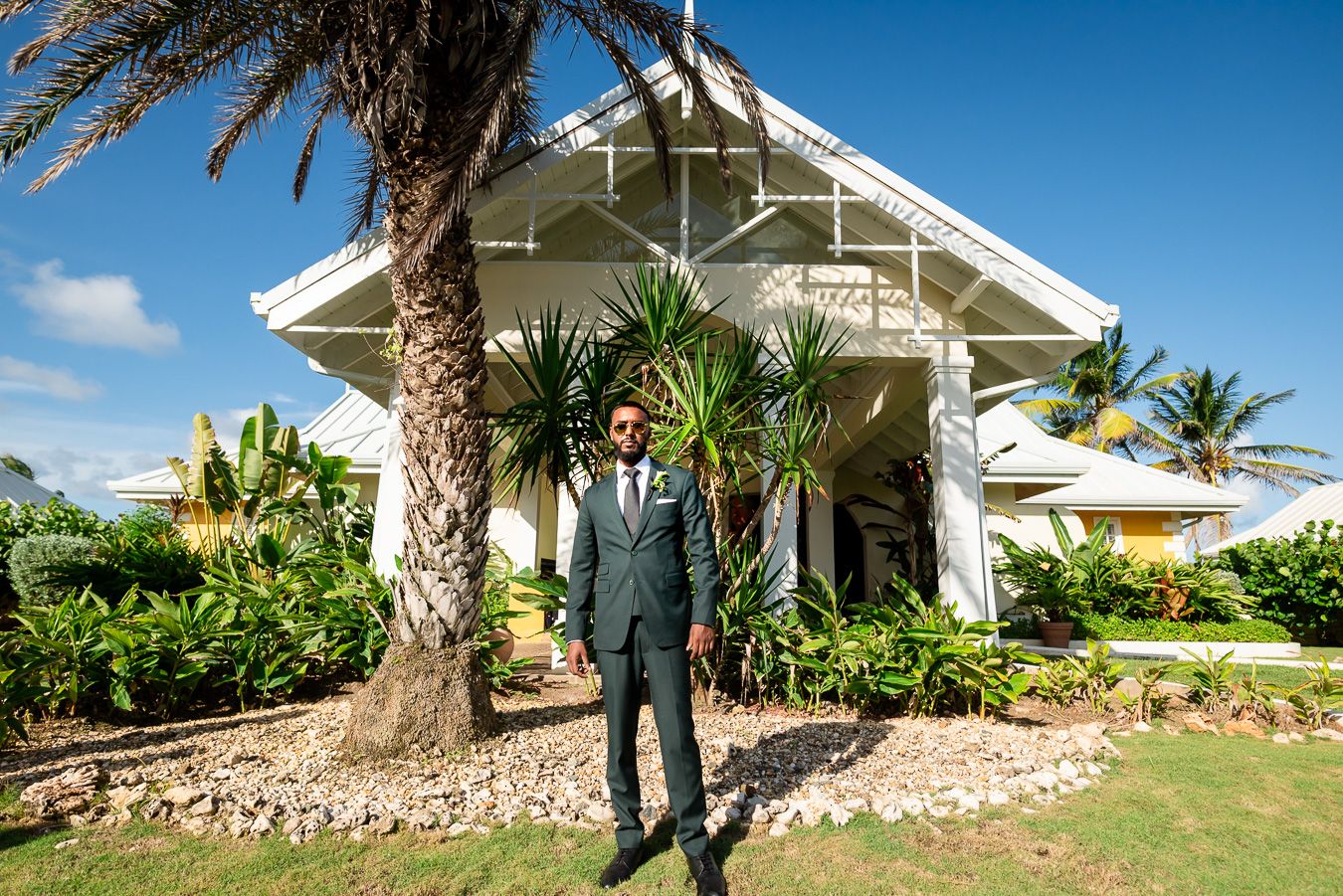 Wedding venue exterior shows white chapel architecture against blue sky and tropical landscaping.