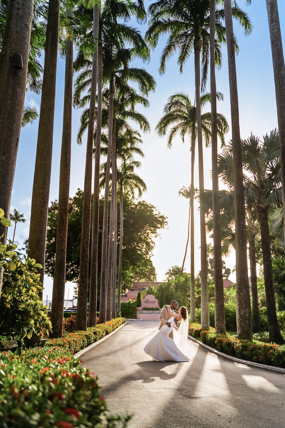 Two people walk down a stunning palm-lined path at a tropical resort during sunset.