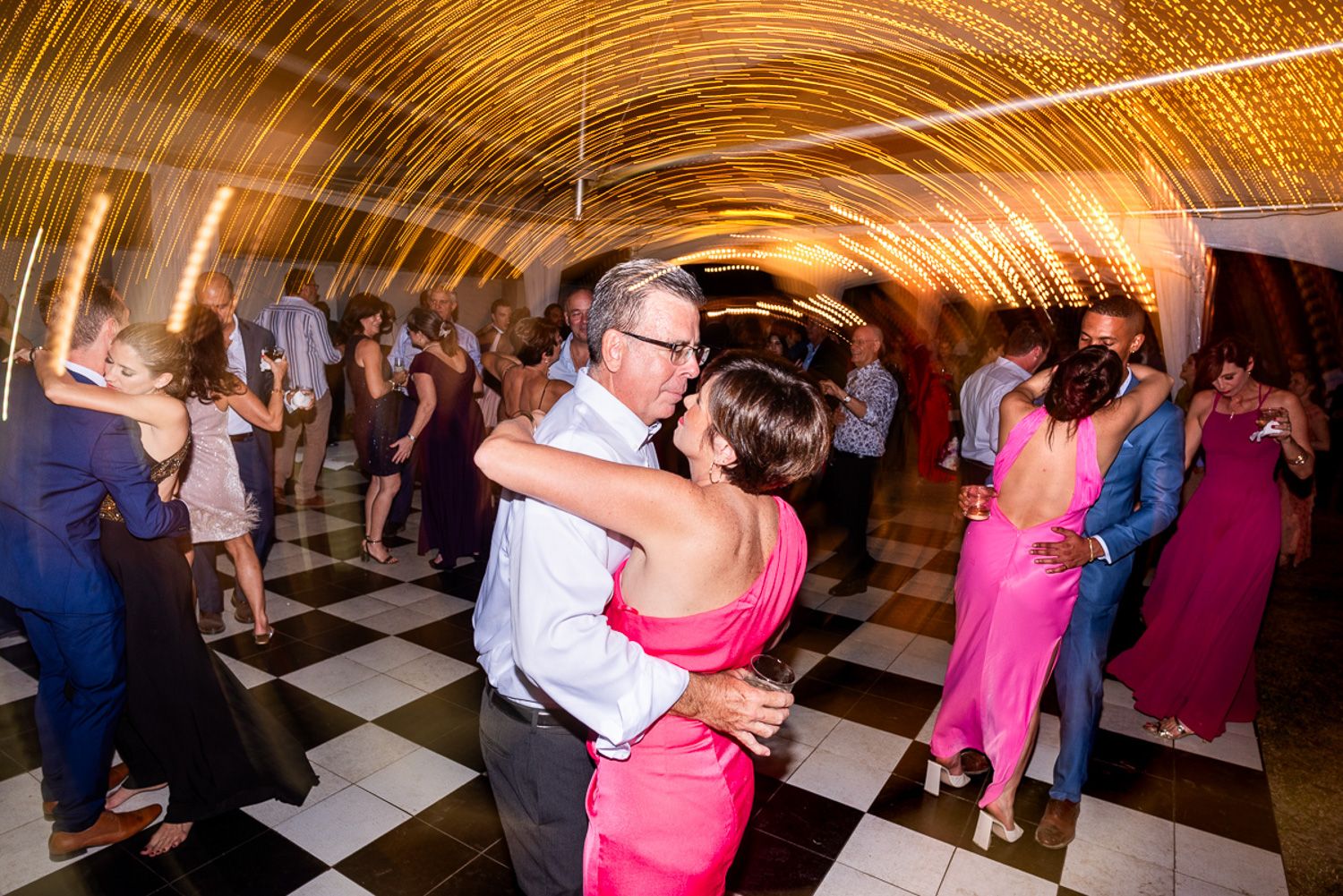 Wedding reception dance floor illuminated with spinning light trails creating virtual golden tunnels effect.