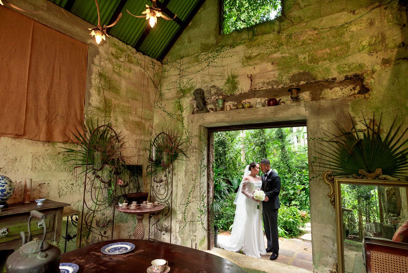 Romantic wedding moment in rustic stone room with hanging plants and natural lighting.