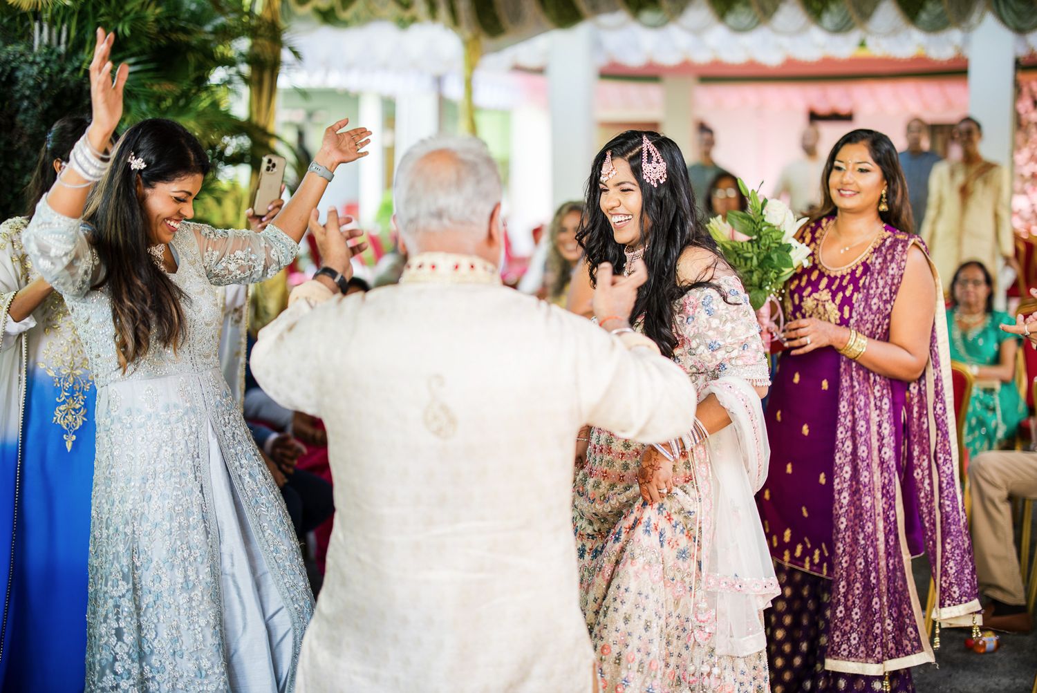 Guests in colorful traditional Indian attire dance joyfully at a vibrant outdoor wedding celebration.