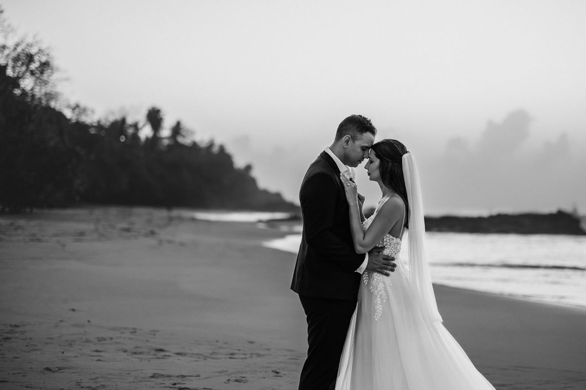 Black and white photo of a bride and groom sharing an intimate moment on a beach at sunset.