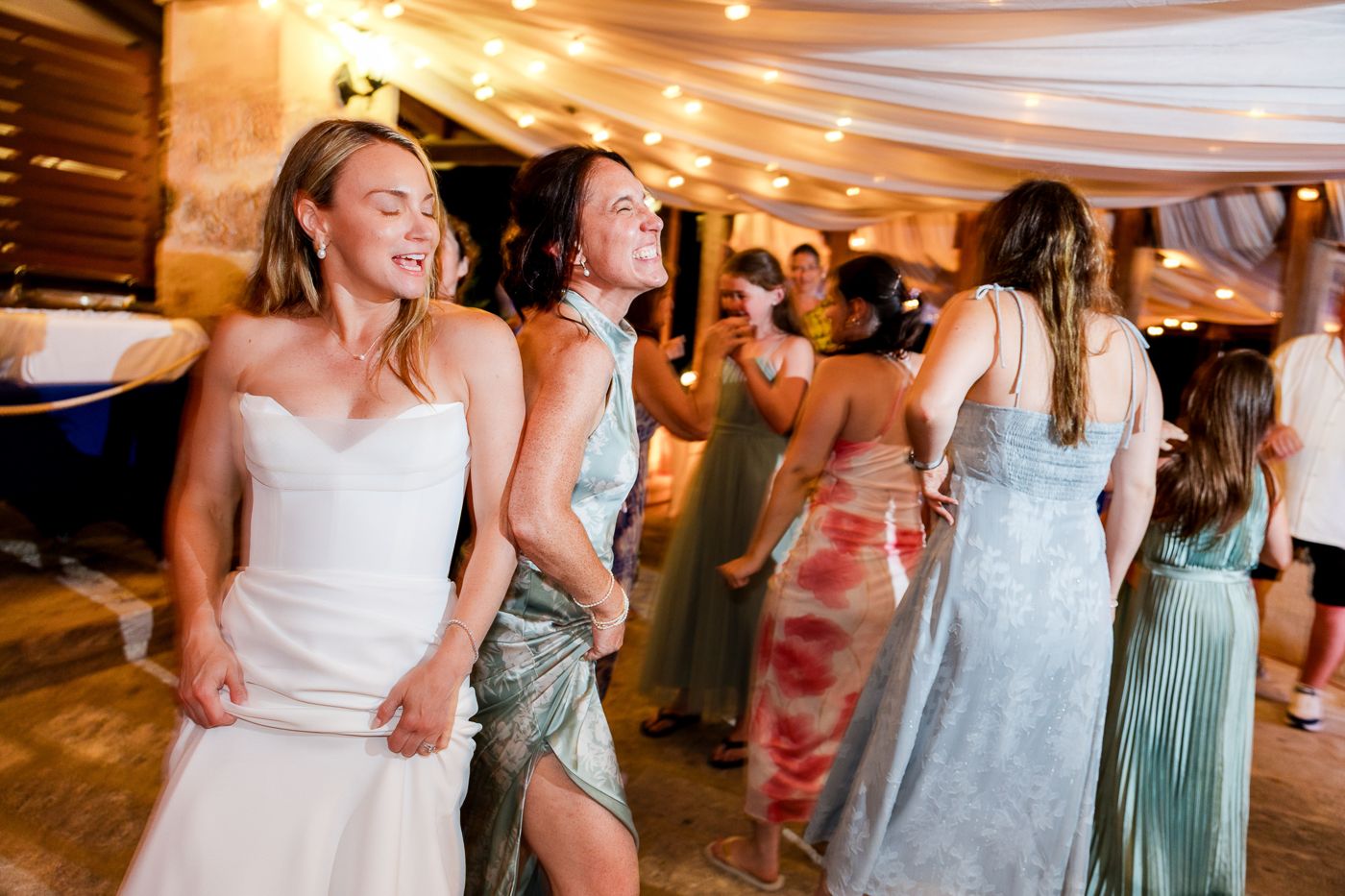 Bride in white strapless gown dancing joyfully with bridesmaids at a festive wedding reception.