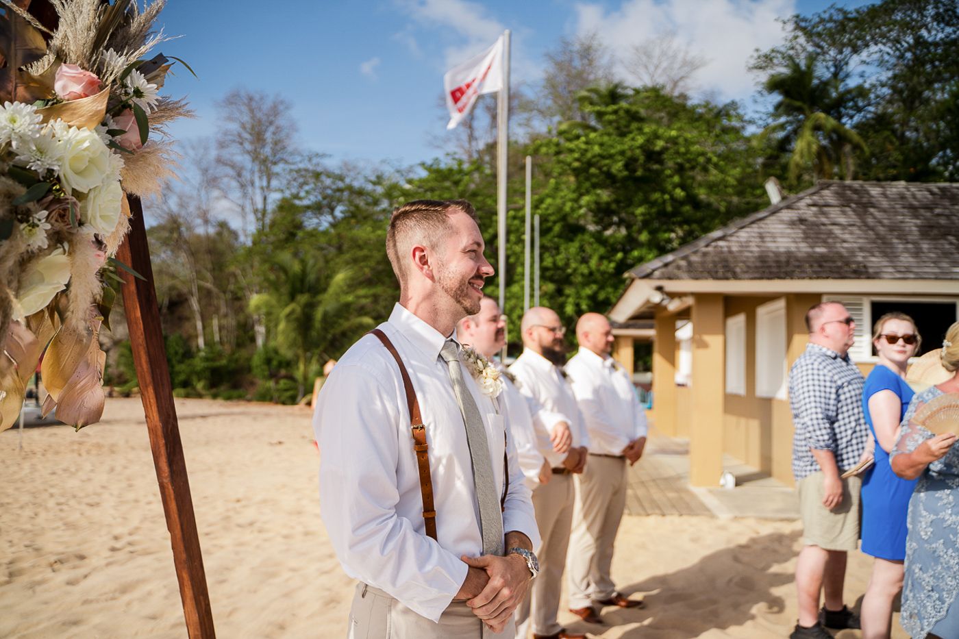 Wedding guests gathered on a sunny beach path with palm trees and ocean views.
