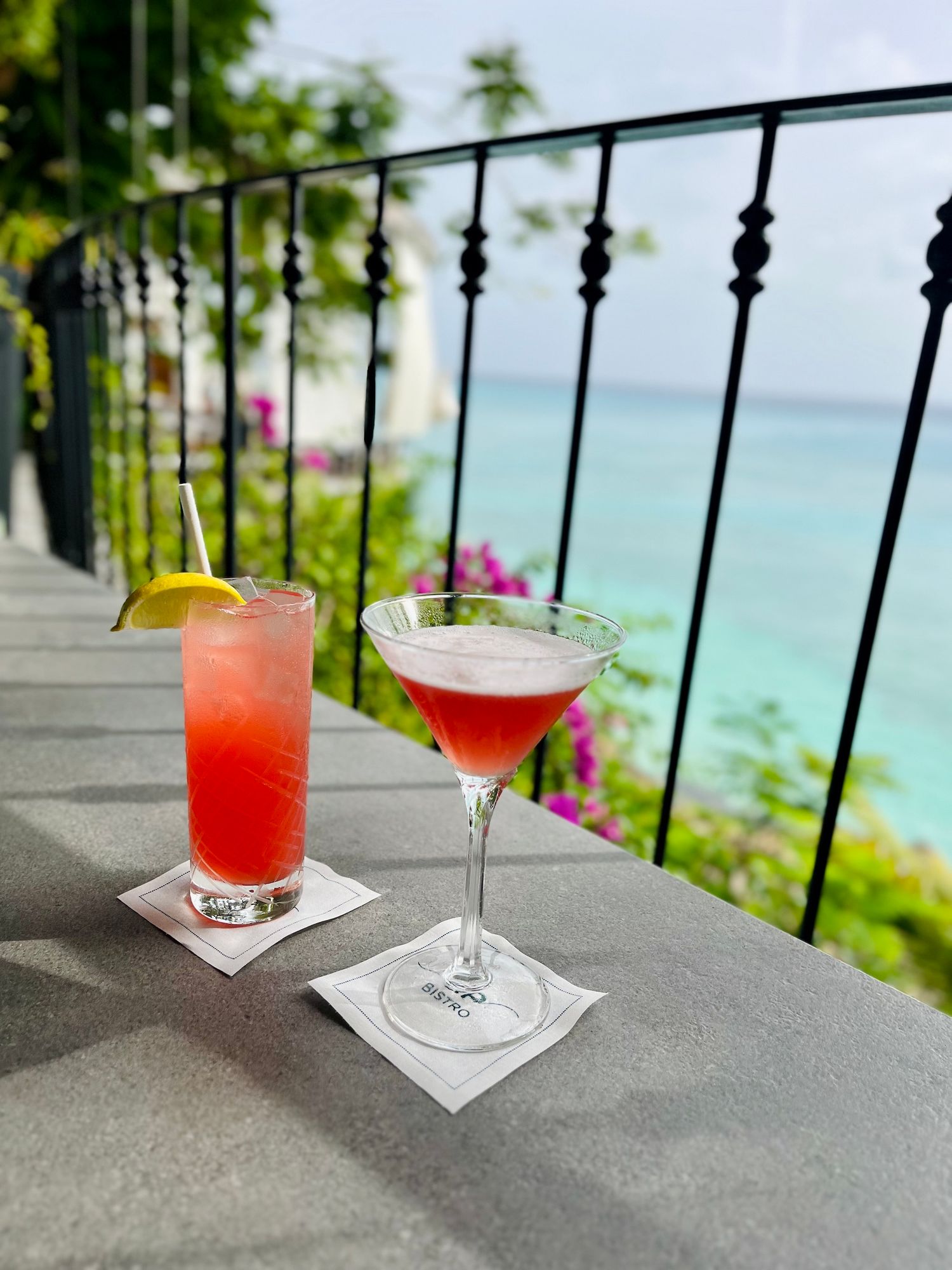 Tropical cocktails displayed on a balcony with ocean views and decorative iron railings. QP Bistro in barbados