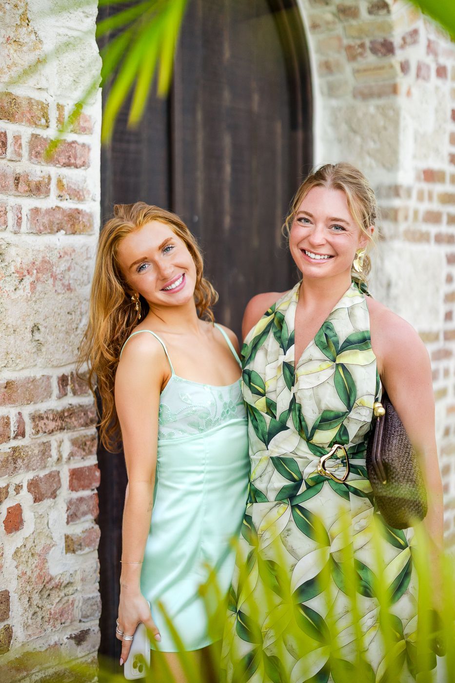 Summer dresses complement the rustic brick wall backdrop at an outdoor venue.