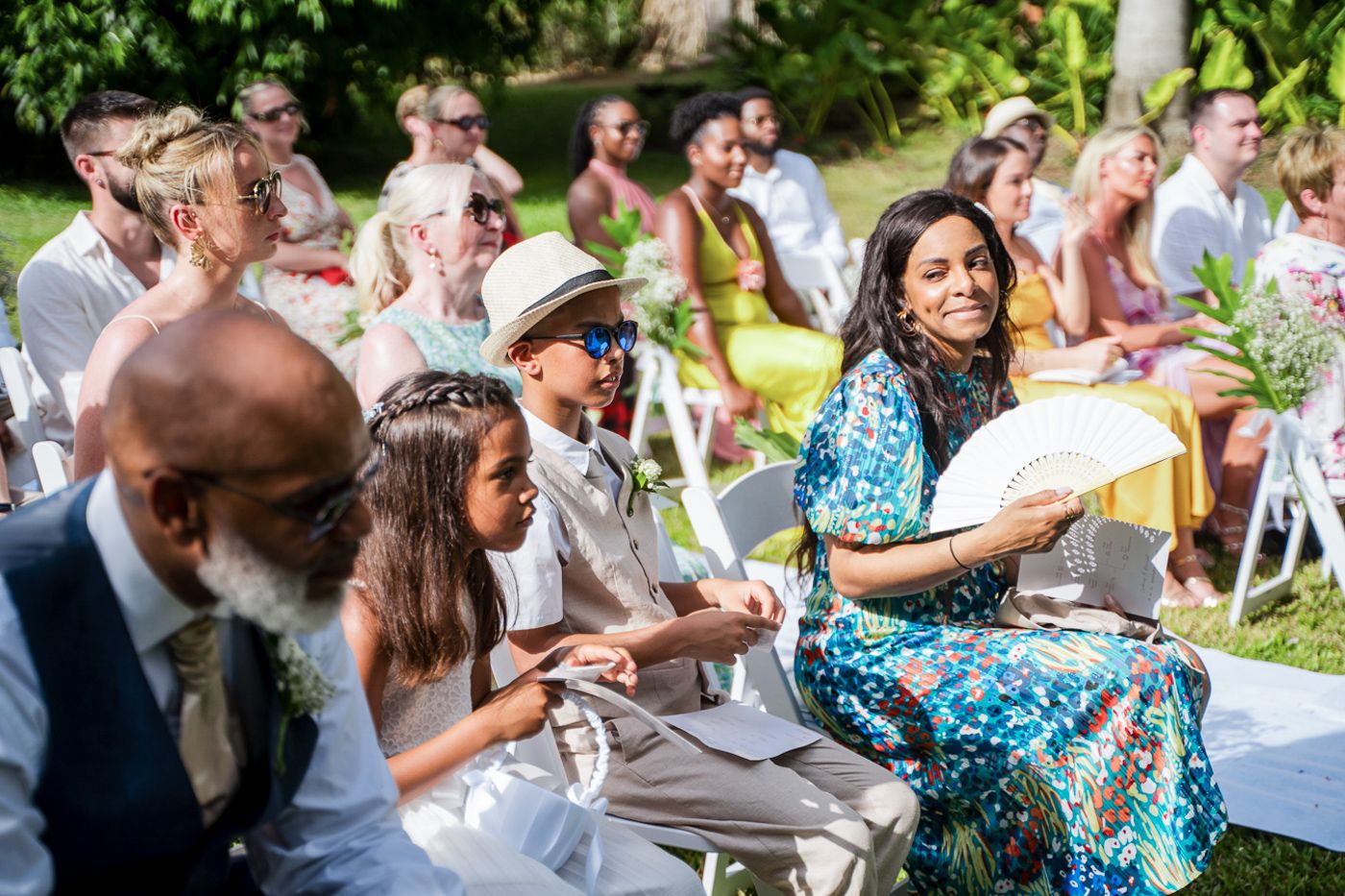 Wedding guests seated in white chairs enjoying an outdoor garden ceremony.