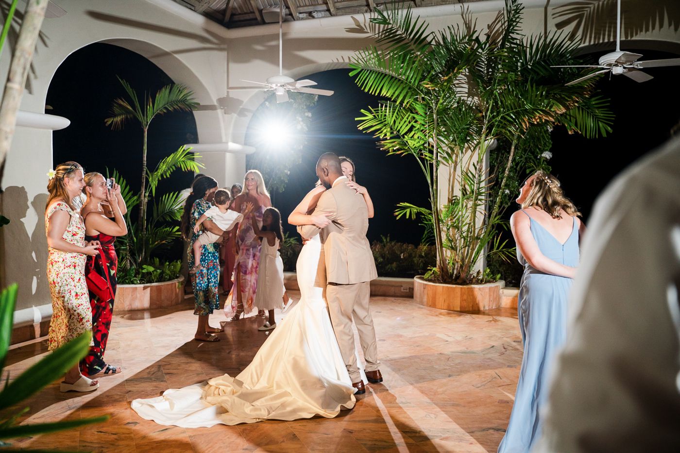 Wedding reception dance scene with couples dancing under arched columns and palm trees.