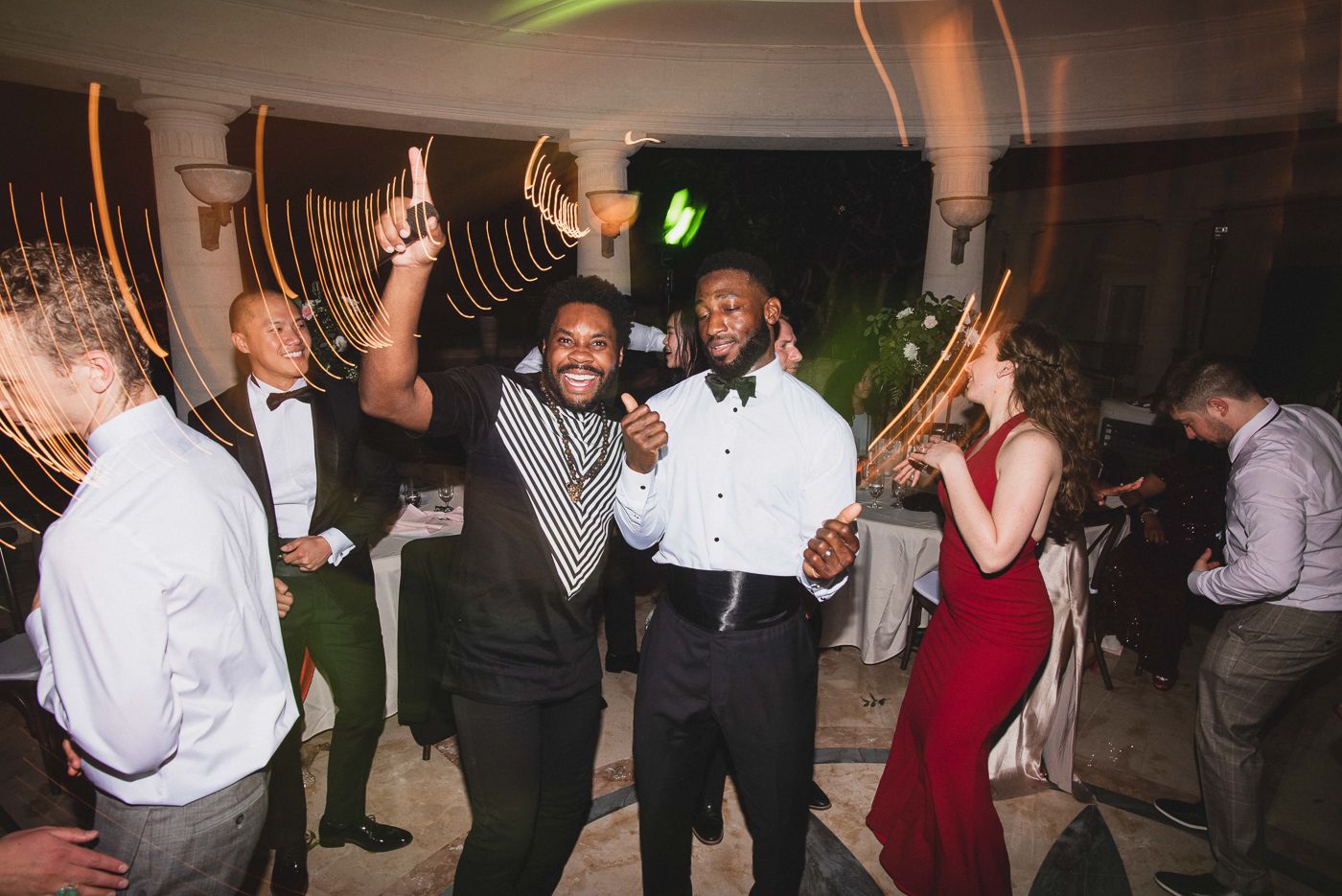 Wedding guests celebrating and dancing under ambient lighting at an indoor reception.