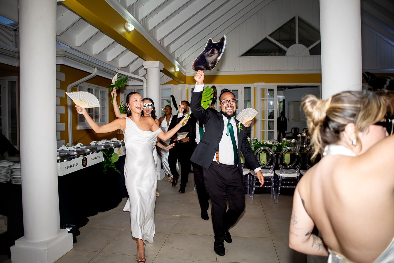 Wedding party dancing and celebrating in elegant columned reception venue.