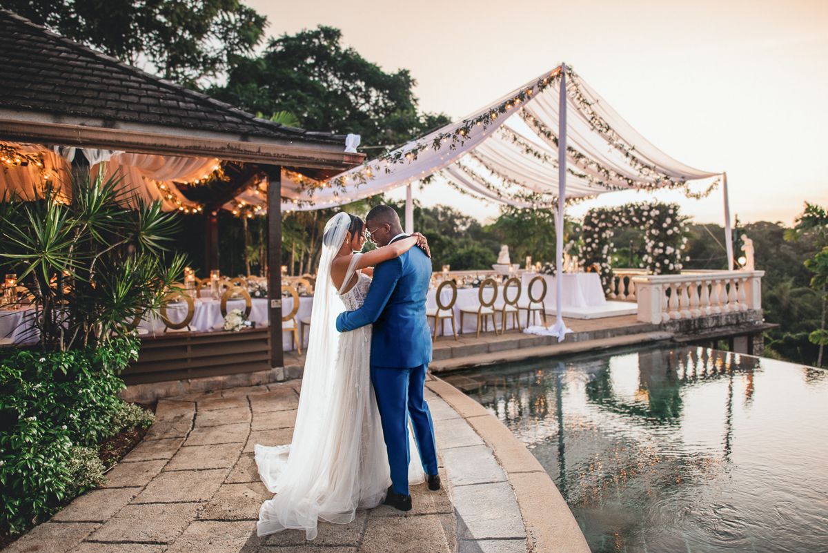 Couple dancing on an outdoor patio under string lights at sunset with tropical foliage in the background.