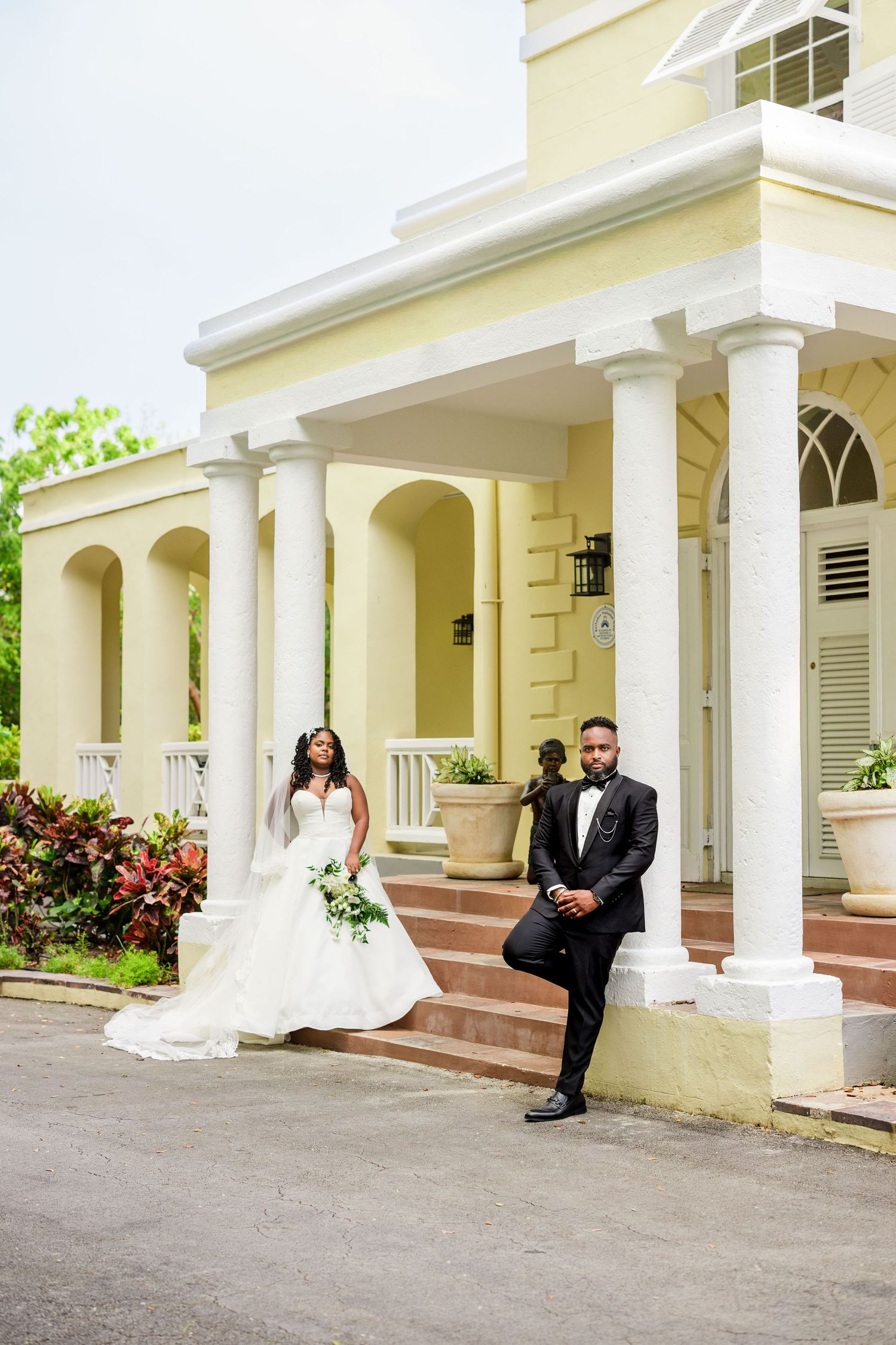 Elegant bride and groom posing outside a yellow colonial mansion with white columns on their wedding day.