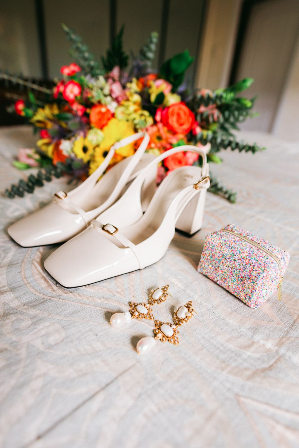 A sequence of elegant white bridal shoes displayed with colorful floral arrangements and delicate accessories on lace fabric.