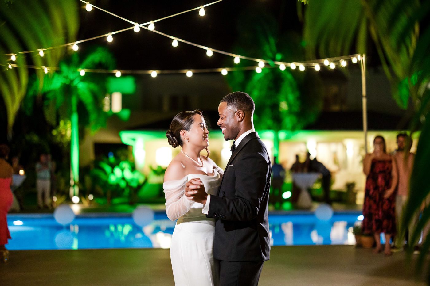 Couples share intimate dances under string lights at a tropical evening wedding reception.