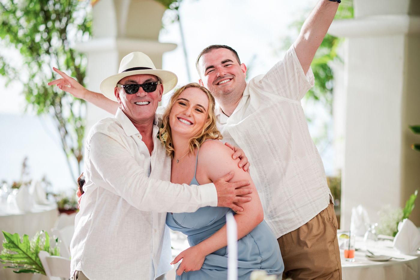 Three people celebrate with joyful expressions and raised arms on a sunny patio.