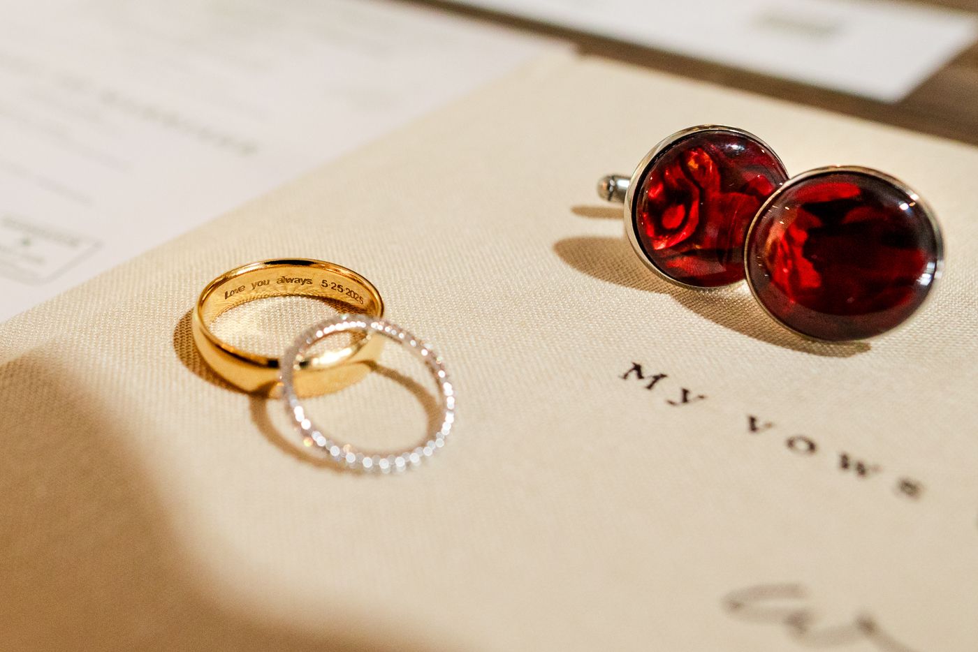 Wedding rings and red cufflinks arranged on cream colored paper in natural light.